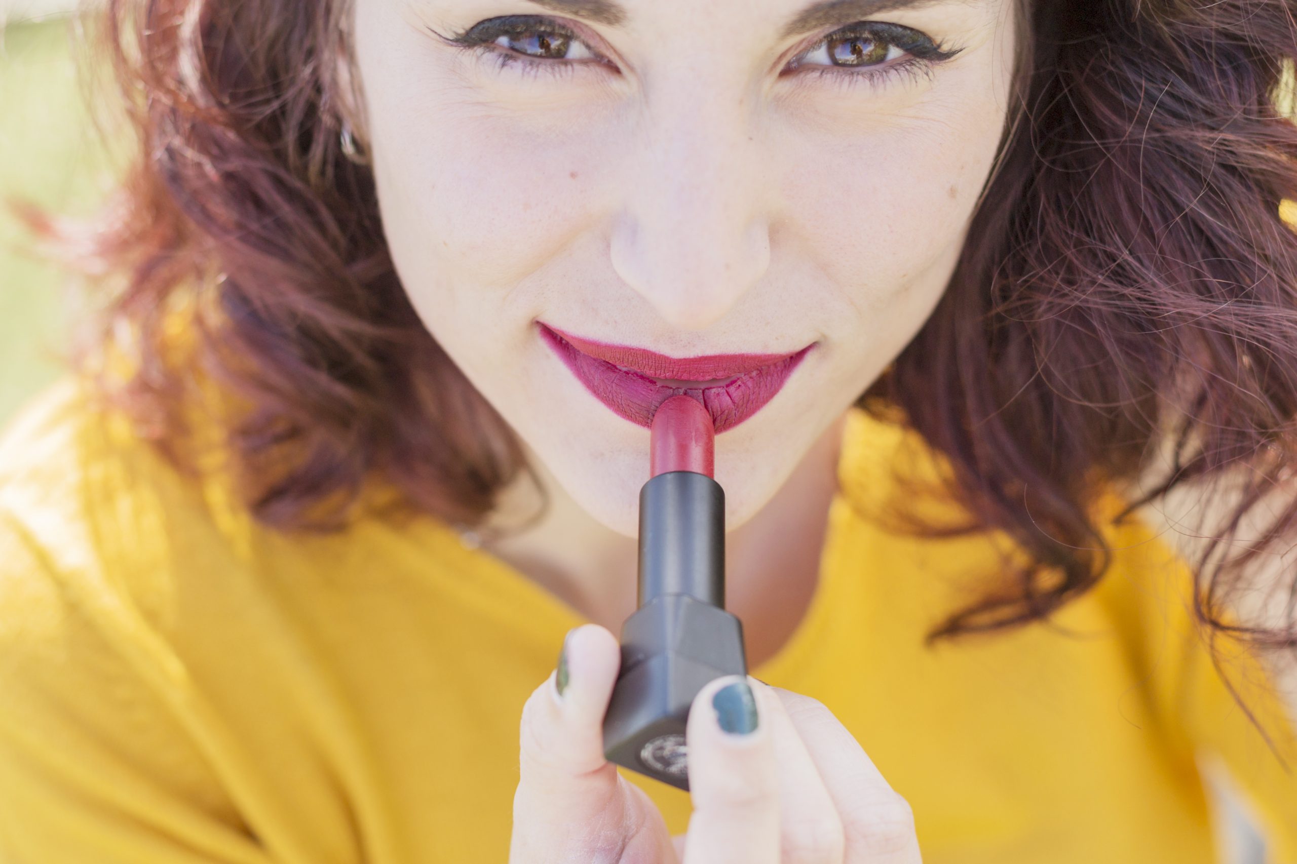 Woman applying glossy berry-red lipstick to her lips.