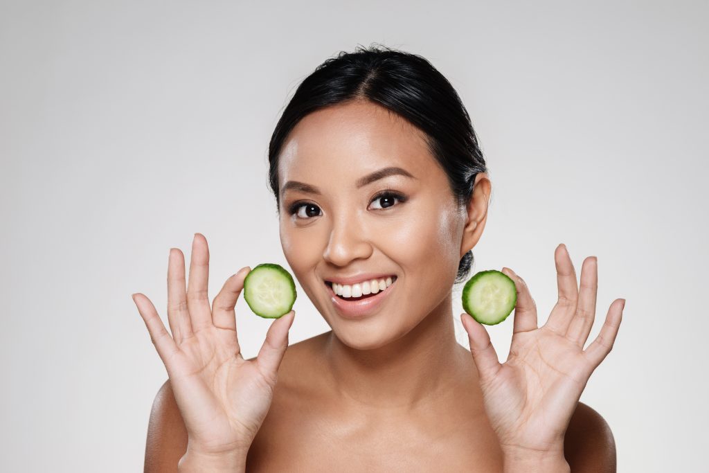 Woman holding cucumber slices as part of natural remedies to get rid of black neck and soothe irritated skin.