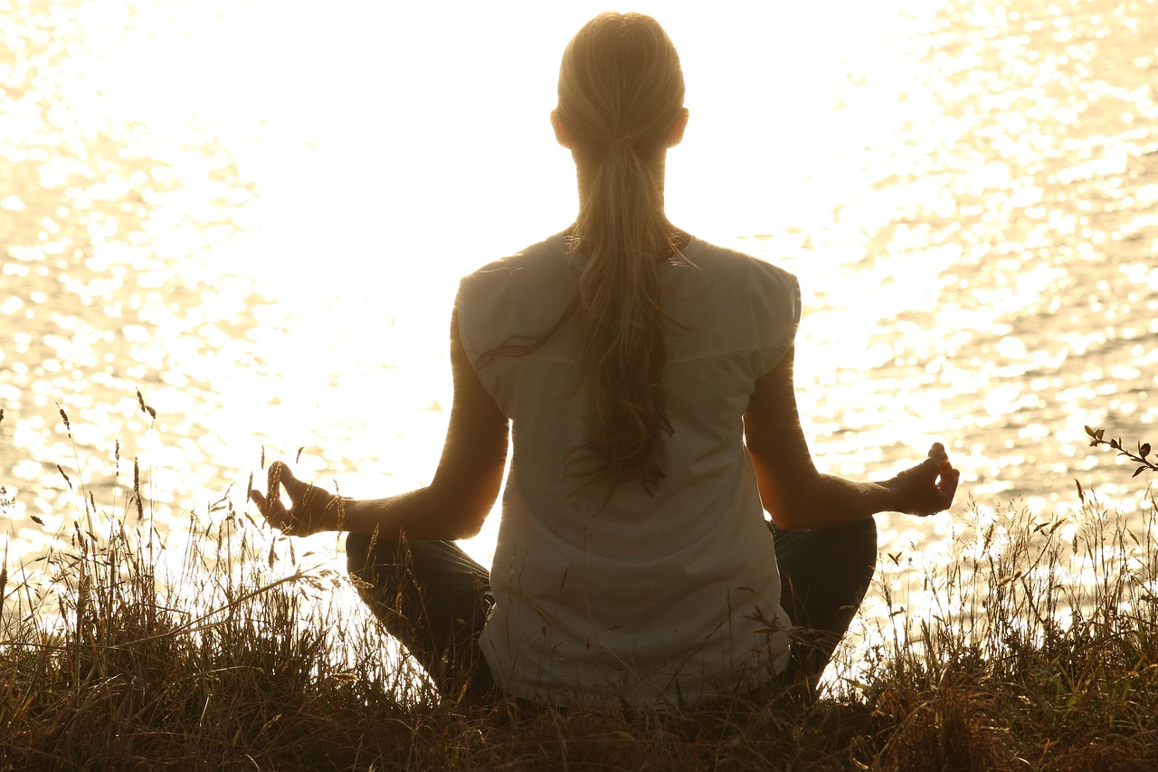 Person practicing mindfulness meditation for mental well-being and happiness in peaceful natural setting
